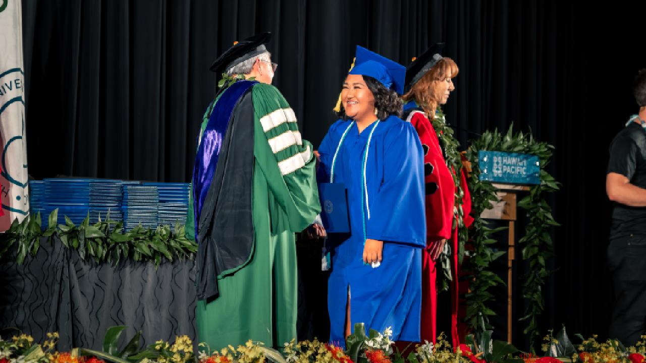 Image of student in cap and gown receiving diploma from University admin